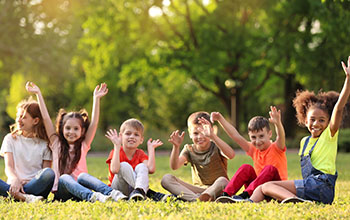 Cute little children sitting on grass with hands in the air outdoors on sunny day