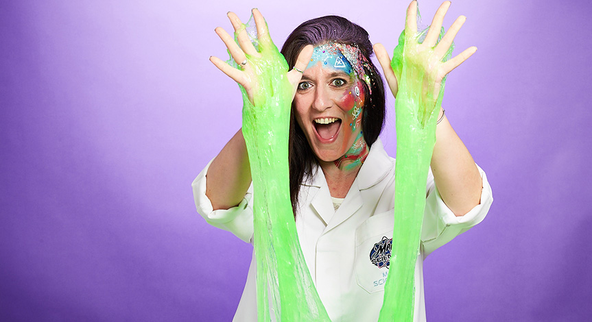 Mad scientist with glitter face paint holding hands in the air with slime dripping down.