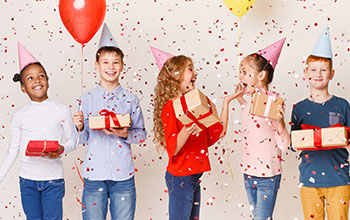 Kids celebrating birthday holding balloons and presents wearing birthday hats with confetti falling over white background