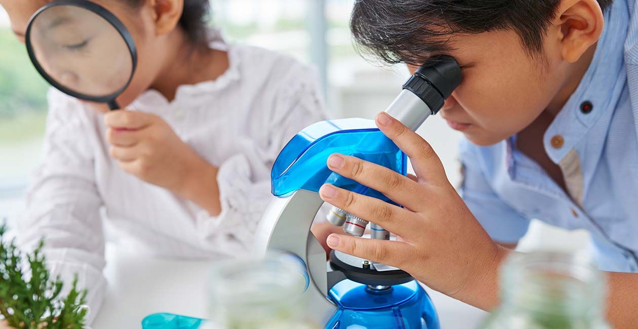 A boy looking through a microscope and a girl looking through a magnifying glass